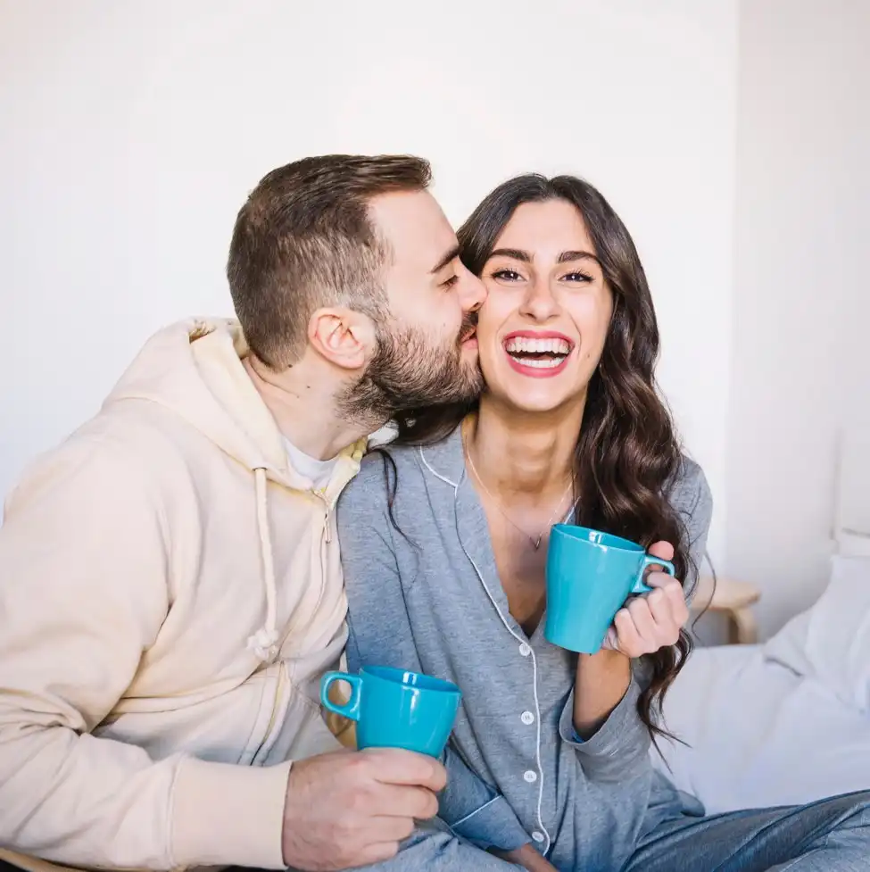 Pareja dándose un beso en la mejilla mientras disfrutan de un café por la mañana en su cuarto de su nueva casa en Exe.